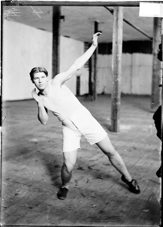 Athlete, E. E. Parry, standing in shot-putting stance in an empty room - Chicago Daily News, Inc.