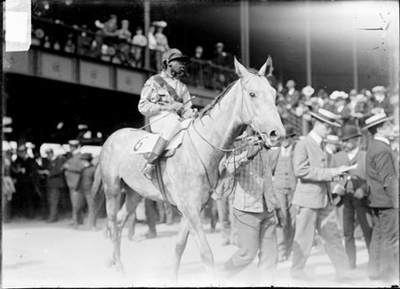 Racehorse, Copper, with African American jockey mounted, being led across paddock by grandstand - Chicago Daily News, Inc.
