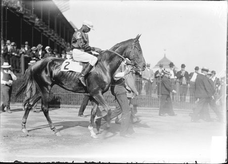Racehorse, Toah, with African American jockey mounted, being led by handler across paddock, Washington Park Race Track - Chicago Daily News, Inc.