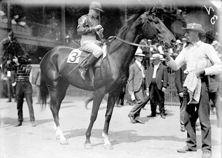 Racehorse, Mary Glenn, with mounted jockey, standing with handler in paddock area - Chicago Daily News, Inc.
