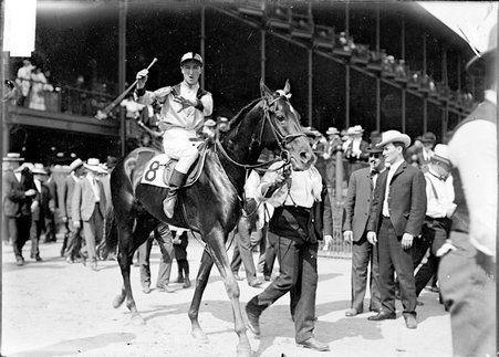 Racehorse, Love Sidney C, with mounted jockey, being led by handler through paddock - Chicago Daily News, Inc.