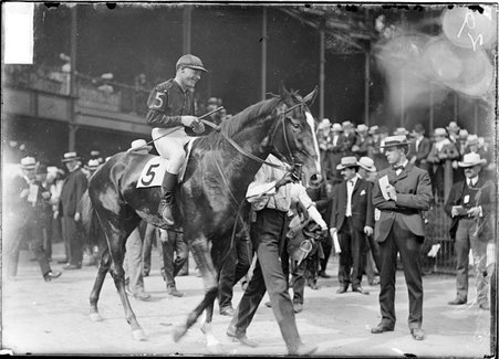 Racehorse, English Lad, with jockey mounted, being led past horsemen in paddock by grandstand, Washington Park Race Track - Chicago Daily News, Inc.