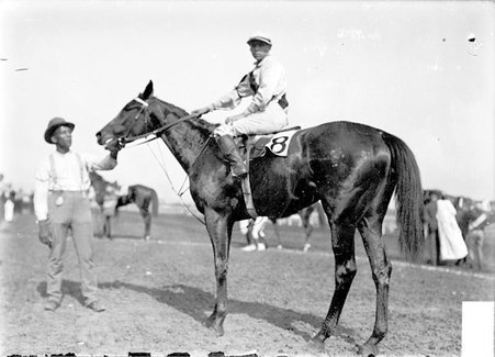 Racehorse, Monarka, with jockey mounted, and African American handler holding its bridle, Washington Park Race Track - Chicago Daily News, Inc.
