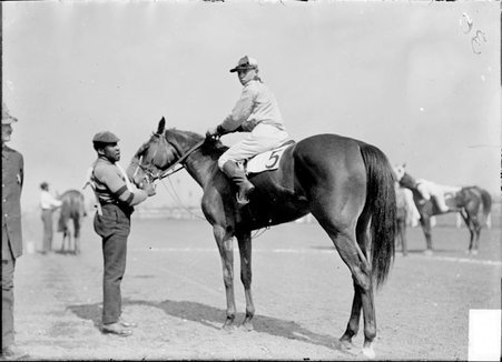 Racehorse, Else L, with African American jockey and handler, standing on racetrack - Chicago Daily News, Inc.