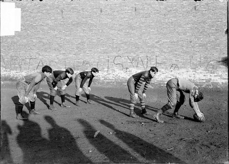 Football team, West Division High School, snapping the ball, five players by brick wall - Chicago Daily News, Inc.