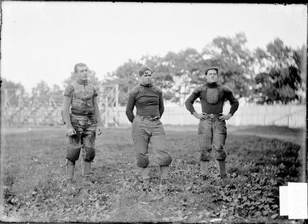 Football team, Northwestern University, three players standing near bleachers on an athletic field - Chicago Daily News, Inc.