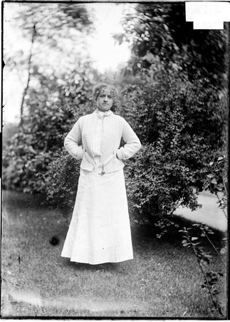 Tennis player, Miss May Sutton, standing, facing camera, near hedge row - Chicago Daily News, Inc.