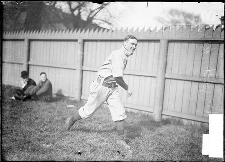 Baseball player, Offergelt, University of Illinois, throwing a ball, warming up near wooden fence - Chicago Daily News, Inc.