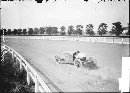 Motorist, Barney Oldfield, driving in racing car along track - Chicago Daily News, Inc.