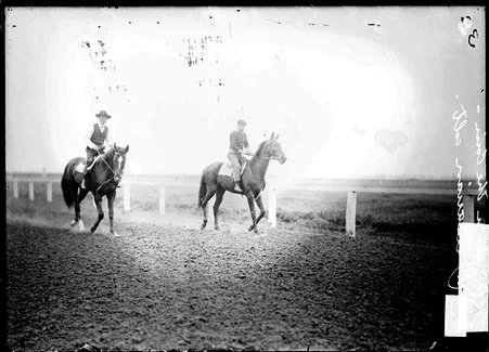 Racehorse, Prince of Cain, with rider mounted, trotting on racetrack beside another horse and rider - Chicago Daily News, Inc.