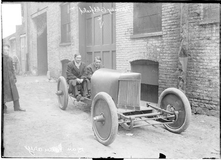 Motorists, Barney Oldfield and Dan Canary, sitting in a car parked next to a garage - Chicago Daily News, Inc.