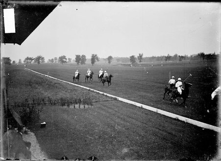 Polo players riding ponies on the field in front of a small two-story metal-roofed building on the sidelines - Chicago Daily News, Inc.