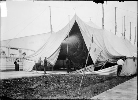 A. Roy Knabenshiue, airship builder, looking at an airship in a tent, men adjusting tent flaps - Chicago Daily News, Inc.