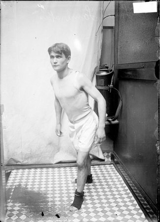 Runner Louis Lambrakes, facing toward left of image, standing in a stairwell hallway in the Daily News building - Chicago Daily News, Inc.
