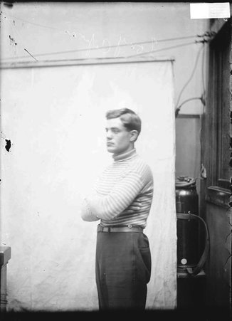 Boxer Tony Caponi, posing with his arms folded across his chest standing with his side to the camera in front of a plain backdrop - Chicago Daily News, Inc.