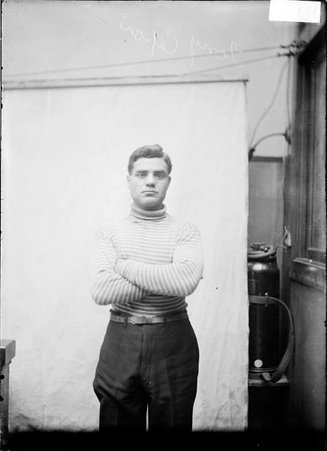 Boxer Tony Caponi, posing with his arms folded across his chest standing in front of a backdrop in a stairwell - Chicago Daily News, Inc.