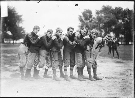 North Division High School football team, seven players, bending forward, standing in a line on an athletic field - Chicago Daily News, Inc.