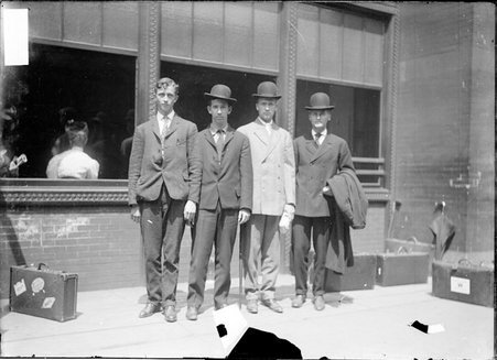 University of Wisconsin crew members, standing outside a train station, a woman's back is visible through window in background - Chicago Daily News, Inc.