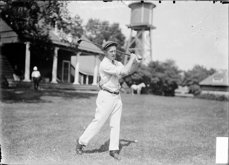 Golfer, Elen Byres, golf club over his shoulder, standing near clubhouse, Wheaton Golf Club - Chicago Daily News, Inc.
