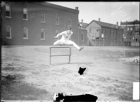 Athlete, E. Hotchkins, jumping over a hurdle on the track at an athletic field - Chicago Daily News, Inc.