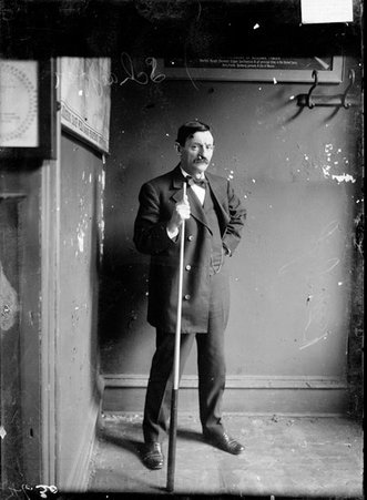 Billiards player Jake Schafer, Sr., holding a cue standing in the corner of a room - Chicago Daily News, Inc.