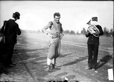 Football player, Blair, Northwestern University, standing on the sideline next to a band member playing a French horn at Marshall Field - Chicago Daily News, Inc.