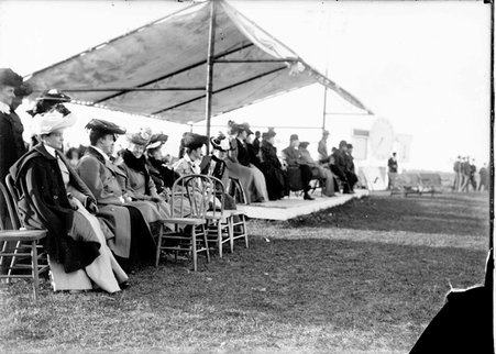 Spectators sitting in chairs under a canopy and on the ground for a polo match at the Onwentsia Country Club in Lake Forest, Illinois - Chicago Daily News, Inc.