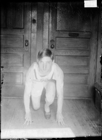 Athlete Harrison, crouching down with his hands in front of him, as if starting a race, in an office, facing forward - Chicago Daily News, Inc.