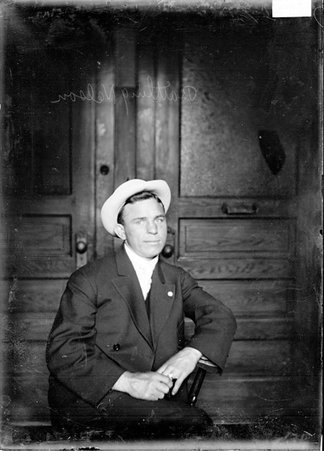 Boxer Battling Nelson, sitting in front of wooden and glass doors in an office, wearing a light colored hat and looking at camera - Chicago Daily News, Inc.