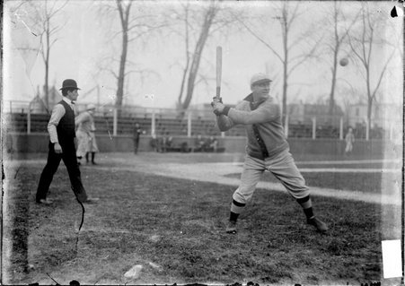 Gunthers baseball player and team captain Nick Pedroes, swinging a bat at a ball in the air in front of him on a baseball field - Chicago Daily News, Inc.