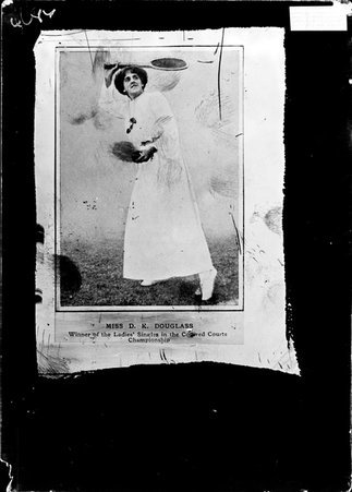 Photograph of ladies' singles champion Miss D. K. Douglass, standing with a racquet above her head on a tennis court - Chicago Daily News, Inc.