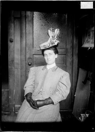 Chess player Mrs. Frank W. Lynn, sitting in a chair in an office, wearing a hat - Chicago Daily News, Inc.