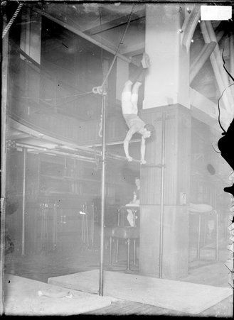 Gymnast standing on his hands on top of a bar in a gymnasium at the YMCA - Chicago Daily News, Inc.