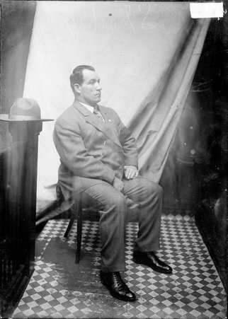 Boxer Tom Sharkey, sitting in a chair in front of a light colored background in a stairwell hallway at the Chicago Daily News building - Chicago Daily News, Inc.