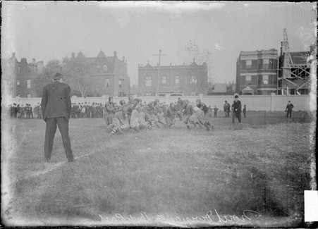 North Division High School and Hyde Park High School football players engaging in a play during a game at an athletic field - Chicago Daily News, Inc.
