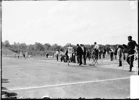 Runner, University of Chicago, James D. Lightbody, running along track past officials - Chicago Daily News, Inc.