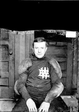 White Eagle football player Red Baker, sitting in a chair in front of wooden doors in an office - Chicago Daily News, Inc.