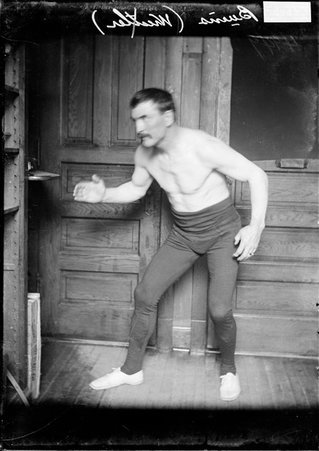 Wrestler Farmer Burns, standing with his knees bent and his arms out in front of him in an office - Chicago Daily News, Inc.
