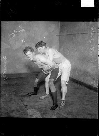 Wrestlers, F. H. Schmitt and A. Bradley, Schmitt holding Bradley around the waist in a wrestling hold in a gymnasium - Chicago Daily News, Inc.