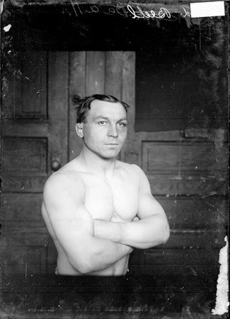 Wrestler, Fred Beell, standing with his arms folded across his chest in a room - Chicago Daily News, Inc.