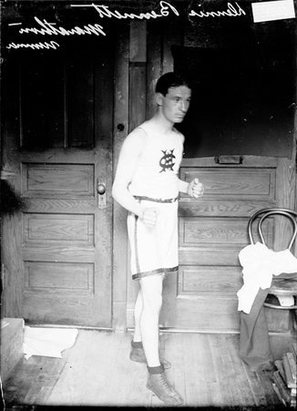 Marathon runner Dennis Bennett, standing in front of wooden doors in an office, facing to right of the image - Chicago Daily News, Inc.