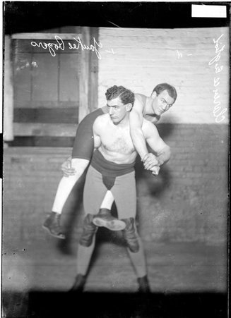 Wrestler, Yankee Rogers, standing, holding Clarence English, a boxer, on his back in a room - Chicago Daily News, Inc.
