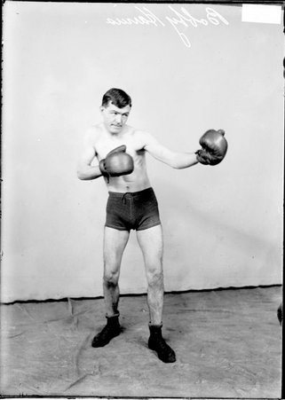 Pugilist Bobby Harris, facing to the right of the camera, standing in a boxing stance in front of a light-colored backdrop - Chicago Daily News, Inc.