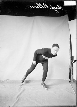 Skater, Hugh Pallicer, leaning over, wearing ice skates in front of a backdrop - Chicago Daily News, Inc.