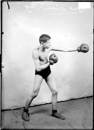 Pugilist, Morie Bloom, throwing a left jab, standing in profile in front of a light-colored backdrop in a room - Chicago Daily News, Inc.