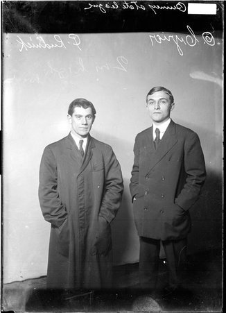 Quincy State League athletes, C. Rudnick and O. Cyrier, wearing street clothes, standing in front of a light-colored backdrop in a room - Chicago Daily News, Inc.