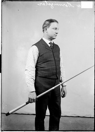 Billiards player, Ora Morningstar, holding pool cue diagonally in front of a light colored backdrop in a room - Chicago Daily News, Inc.