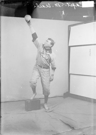 Indoor baseball player, Spalding, M. Searle, reaching arm up, holding ball in front of a backdrop in a room - Chicago Daily News, Inc.