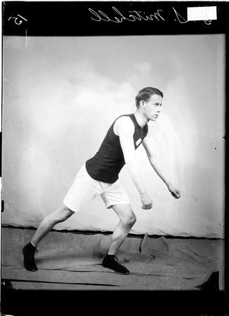 Athlete, G. S. Mitchell, leaning forward with his arms extended in front of him, standing in a ready position in front of a backdrop - Chicago Daily News, Inc.