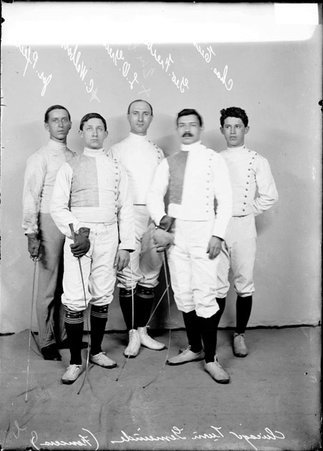 Chicago Turn Gemeinde fencers Pfeil, Eichin, Walbott, Freibert, and Greines, gathered in two rows in front of a backdrop - Chicago Daily News, Inc.